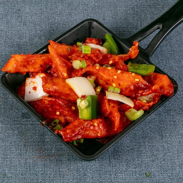 Chili chicken with onions and green peppers in a black square pan on a gray background.