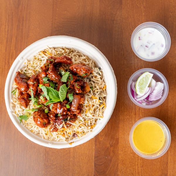 Chicken 65 Biryani with sides of raita, sliced red onions, lime, and yellow sauce.