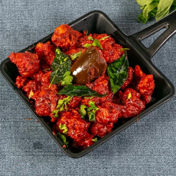 Red chili chicken in a black pan, garnished with green herbs and a dark chili.