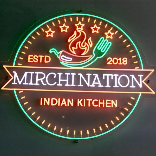 Neon sign for Mirchination Indian Kitchen, featuring a chili pepper, flame, and fork.