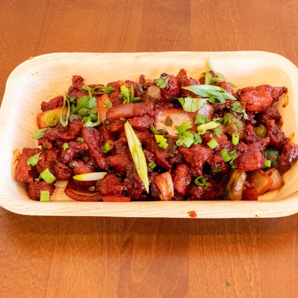 Spicy red chicken chili with green onions and cilantro in a light wooden bowl.