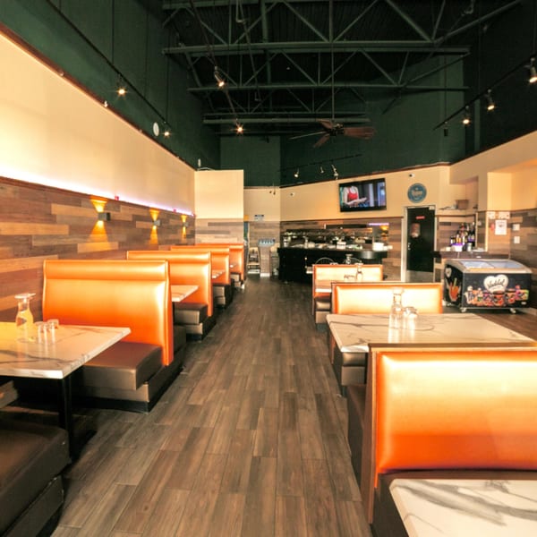 Empty restaurant interior with orange booths, marble tables, wood paneling, and dark wood floors.