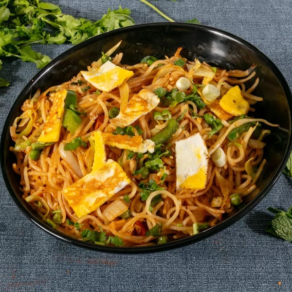 Noodles with scrambled eggs, green onions, and cilantro in a black bowl on a gray surface.