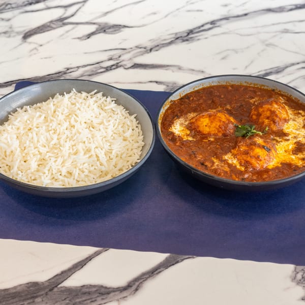 A bowl of white rice next to a bowl of egg curry with a creamy sauce and cilantro garnish.