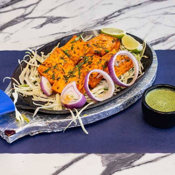 Sizzling paneer tikka with onions, lime, and green chutney on a dark blue and marble surface.