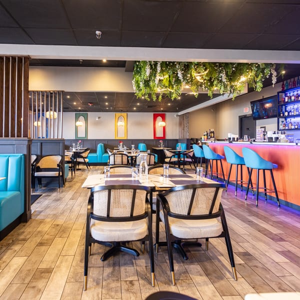 Modern restaurant interior with blue booths, rattan chairs, a bar with blue stools, and hanging greenery.