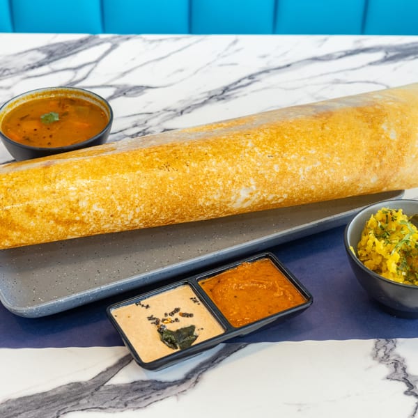 Crispy golden dosa with sambar, potato curry, and two chutneys on a marble table.