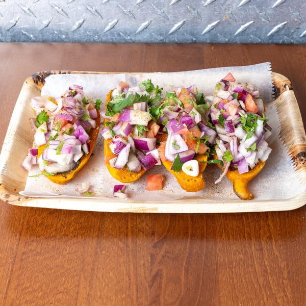 Four golden fried plantain cups filled with diced red onion, white onion, and cilantro on a wooden tray.