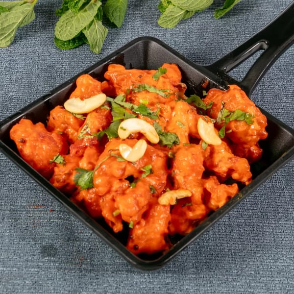 Bright orange chicken 65, garnished with cashews and cilantro, in a black square dish.