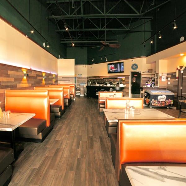 Empty restaurant interior with rows of orange booths, marble tables, and wood-paneled walls.