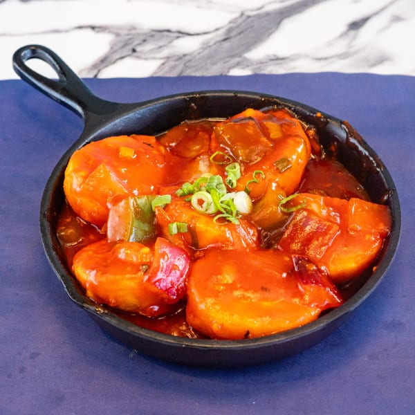 Sweet and sour momos in a black cast iron pan, garnished with chopped green onions.