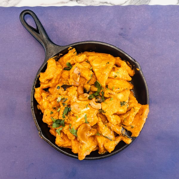 Chicken tikka masala in a cast iron skillet, garnished with cilantro and cashews.