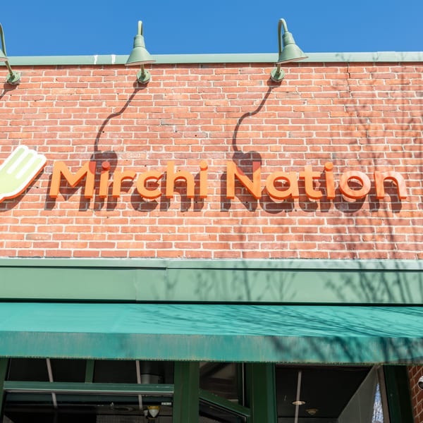 Mirchi Nation restaurant sign with orange letters on a brick wall above a green awning.