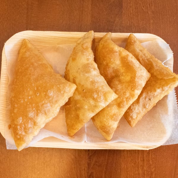 Four golden-brown fried pastries, possibly samosas or empanadas, arranged on a wooden tray with parchment paper.