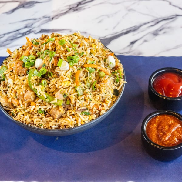 A bowl of fried rice with vegetables and chicken, served with two dipping sauces.