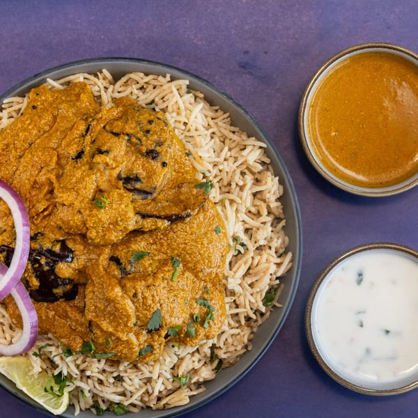 Eggplant curry with rice, red onion, lime, and two side sauces on a purple background.