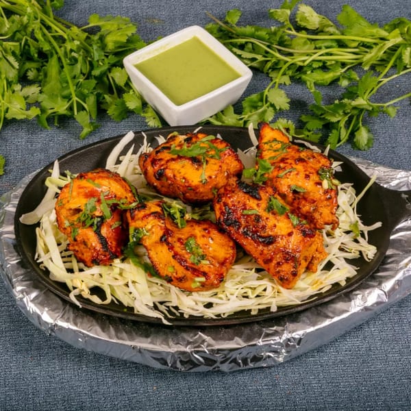 Grilled chicken tikka pieces on a bed of shredded cabbage, with green chutney and cilantro.