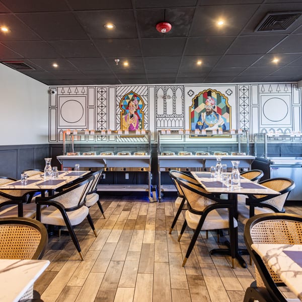 Restaurant interior with buffet stations, modern tables, woven chairs, and colorful wall art.
