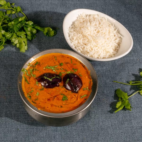 A metal bowl of orange curry with two dark purple eggplants and cilantro, next to a bowl of white rice.