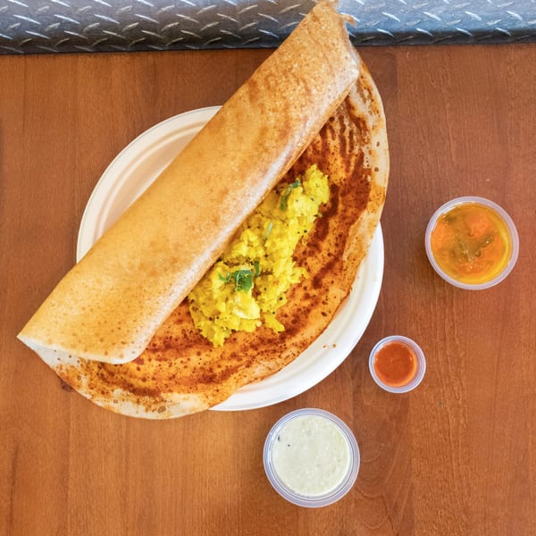 A golden-brown dosa filled with yellow potato masala, served with three small dipping sauces.