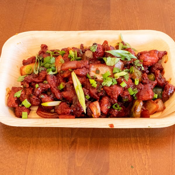 Spicy red chicken chili with green onions and cilantro in a light wooden bowl.