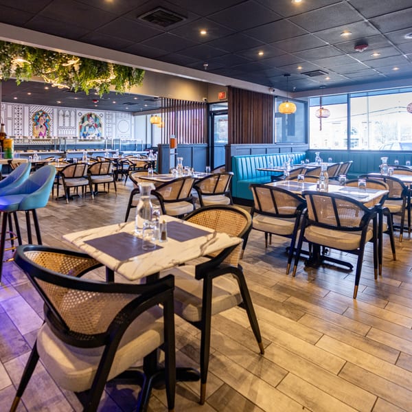 Spacious restaurant interior with modern decor, blue booths, marble tables, and woven chairs.