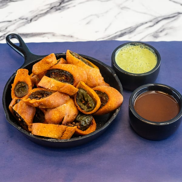 Fried jalapeño poppers in a black skillet, served with green and brown dipping sauces.