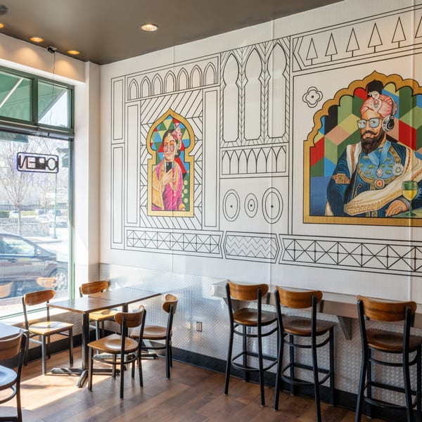 Restaurant interior with colorful murals, tables, chairs, and bar stools, bathed in natural light.