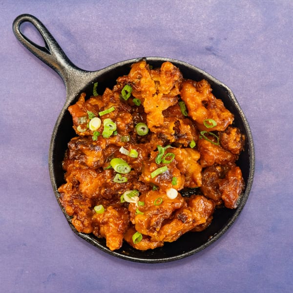 Crispy orange chicken pieces, garnished with green onions, served in a black cast iron skillet.